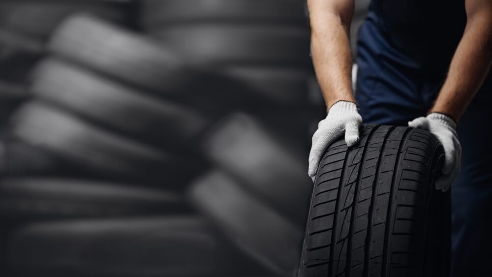 Portrait,Man,Mechanic,Holding,New,Tyre,On,Background,Store,,Car